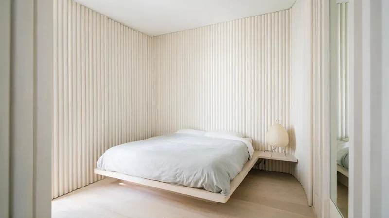 Dormitorio estrecho con el cabecero revestido en panel acanalado claro cuyas líneas verticales estiran la habitación